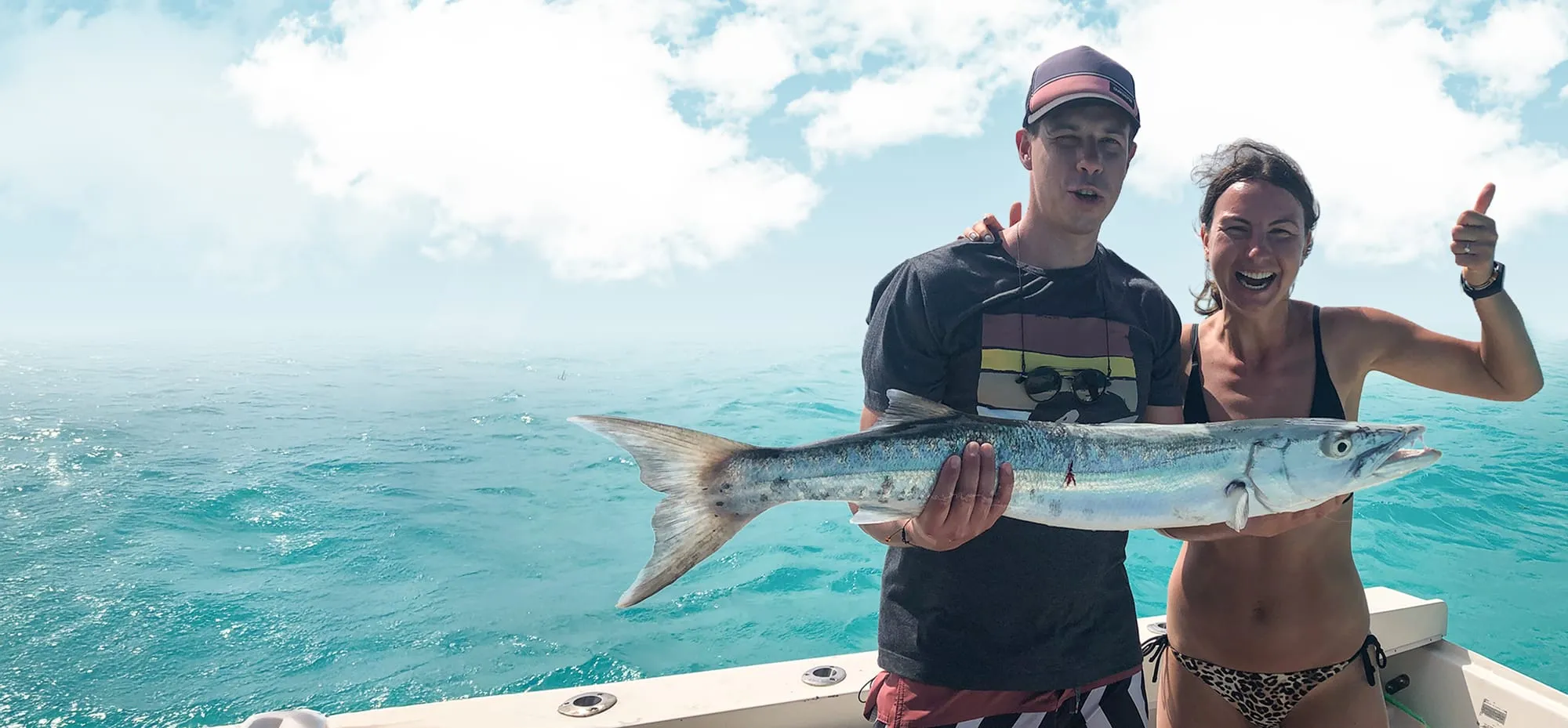 Two anglers holding a big barracuda on the water